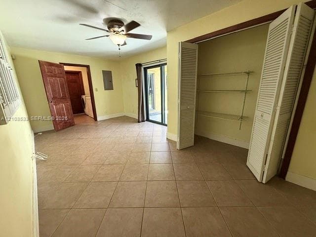 Room featuring square ceramic tile flooring, a ceiling fan with integrated lighting, bi-fold louvered closet doors with adjustable shelving, and a glass sliding door