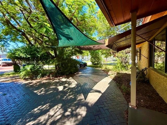 Herringbone-patterned brick paver patio featuring a fixed porch support column, metal awning, and triangular overhead shade sails
