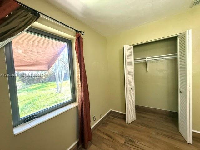 Wood-finish flooring, metal-frame casement window with tile sill, and closet featuring white louvered doors