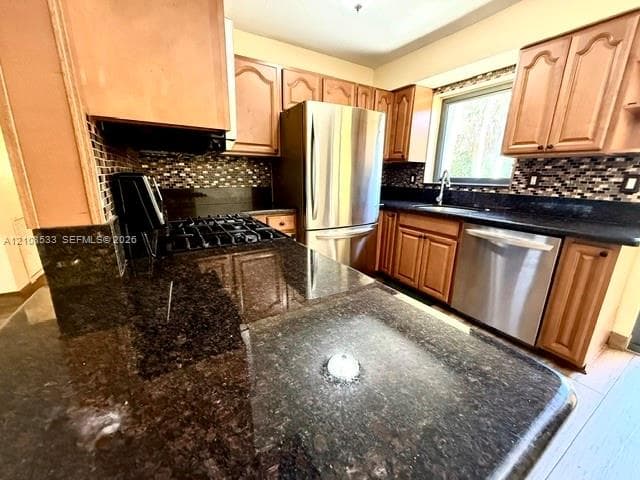 Kitchen featuring natural wood cabinetry, stone countertops, mosaic tile backsplash, and stainless steel appliances