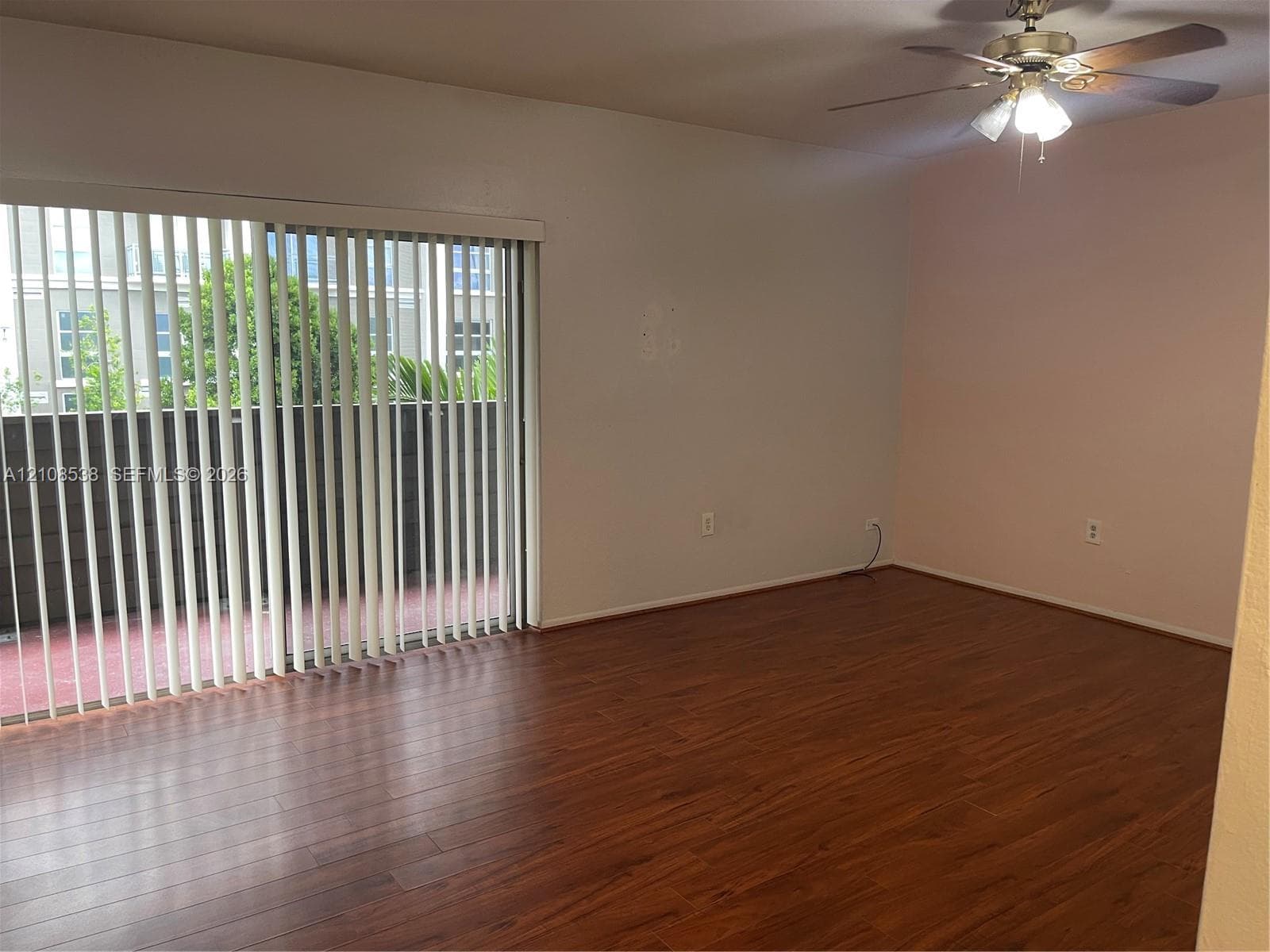 Room featuring wood-finish flooring, a ceiling fan with integrated lighting, and a large sliding glass door with vertical blinds