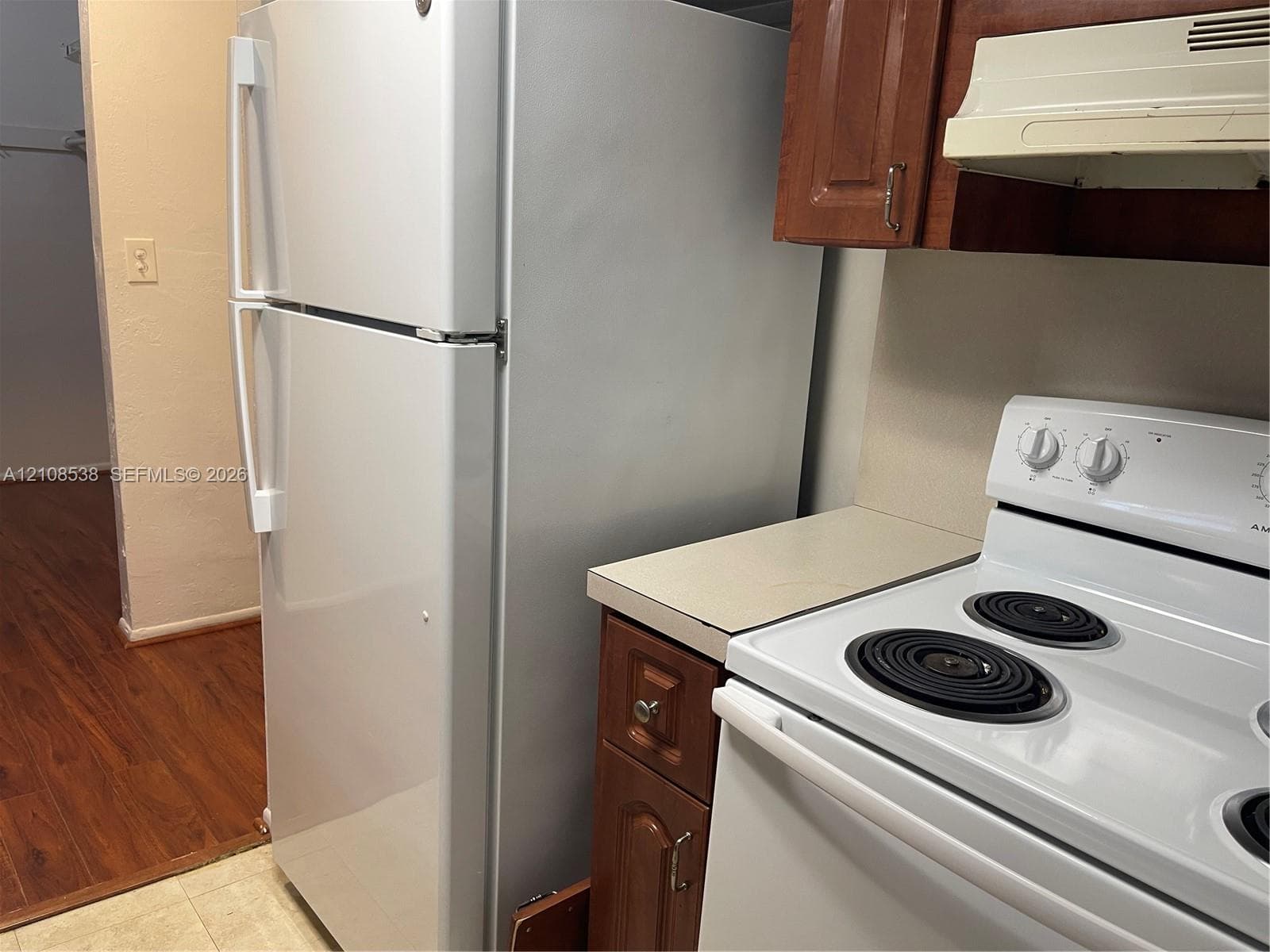 Kitchen featuring a white top-freezer refrigerator, electric range with coil burners, white range hood, wood-finish cabinetry, and solid-surface countertop