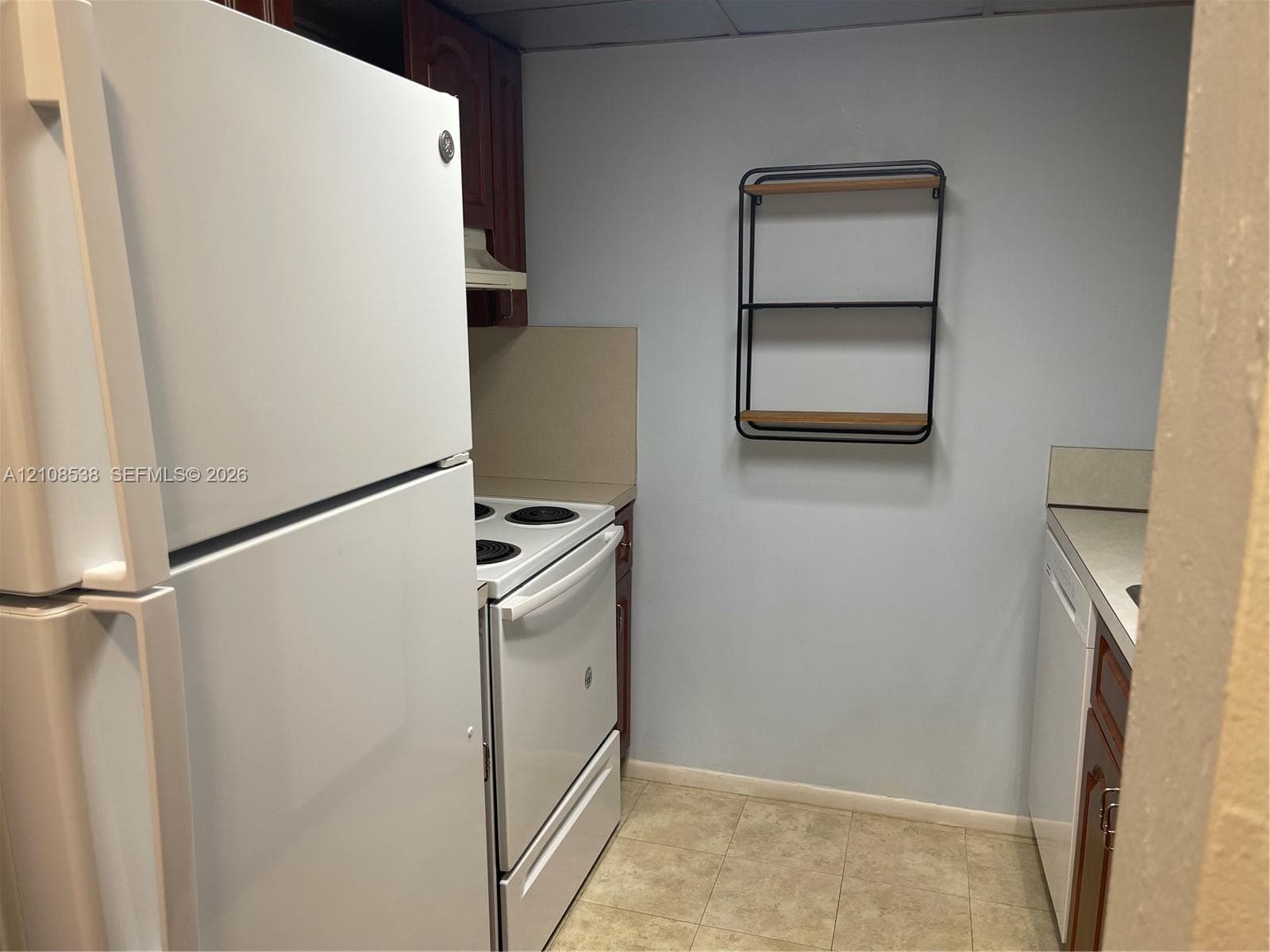 Kitchen featuring white appliance suite including a refrigerator, electric range, and dishwasher, paired with wood-finish cabinetry and neutral tile flooring