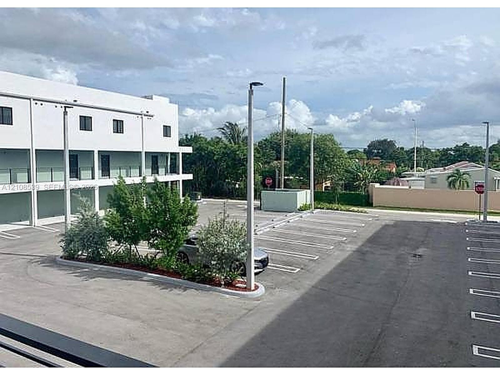 Multi-story building featuring a paved parking area, ground-level covered spaces, exterior lighting fixtures, and manicured landscape islands
