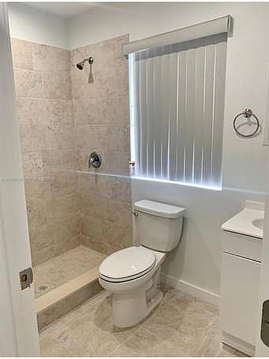 Bathroom featuring a walk-in shower with tiled walls, neutral floor tiling, a white vanity, and a circular wall-mounted towel ring