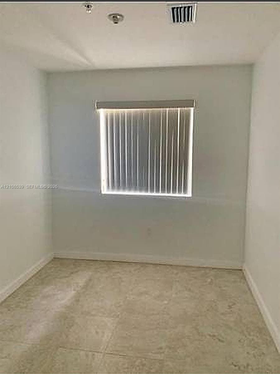 Neutral-toned stone flooring and a single-pane window featuring installed vertical blinds
