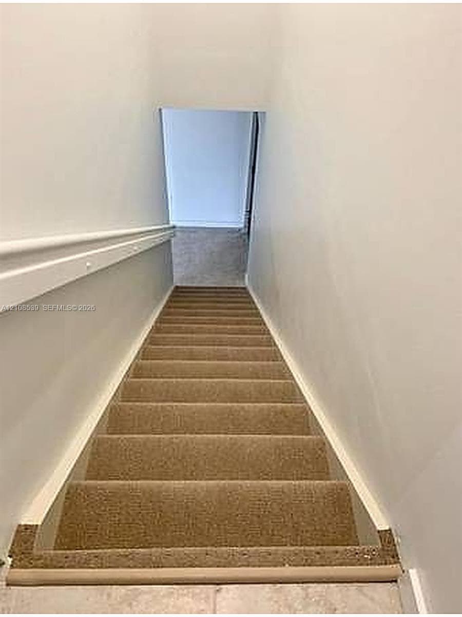 Staircase with neutral-toned carpeting and a fixed wall-mounted handrail