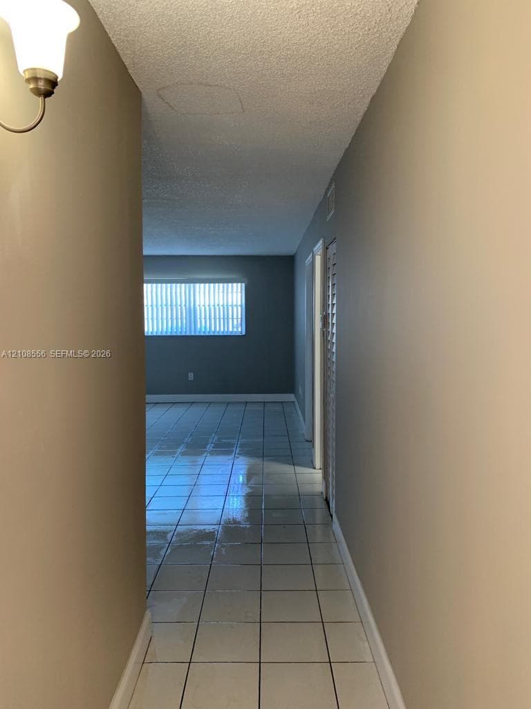 Hallway featuring tile flooring, neutral wall paint, a wall-mounted light fixture, and louvered closet doors