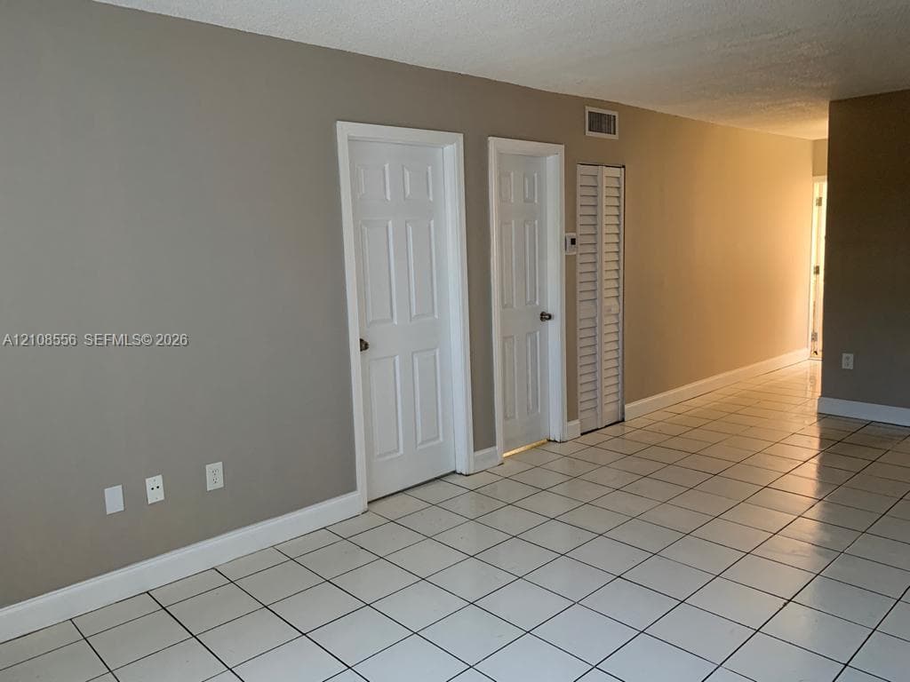 Neutral-toned interior featuring white ceramic floor tile, two interior paneled doors, and a louvered closet door
