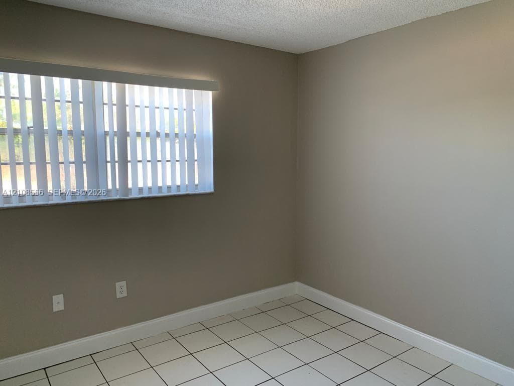 Neutral-toned interior room featuring white tile flooring, vertical window blinds, and textured ceiling finish
