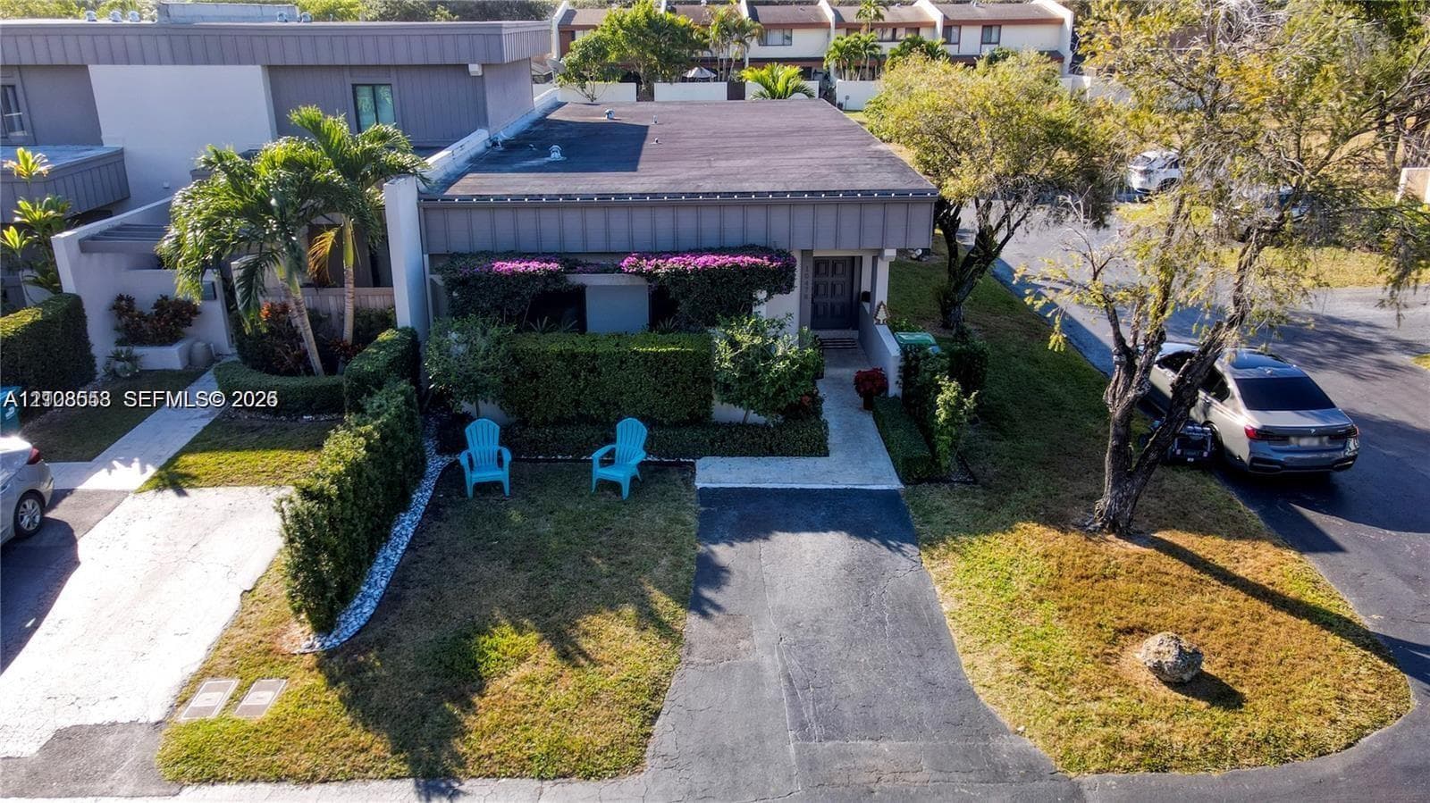 Exterior facade featuring a flat roofline, integrated landscaping, manicured privacy hedges, and a paved private driveway