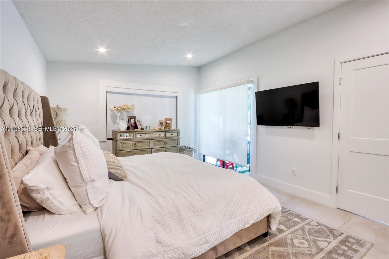 Neutral-toned interior featuring recessed ceiling lighting, light-colored tile flooring, and a sliding glass door with roller shade