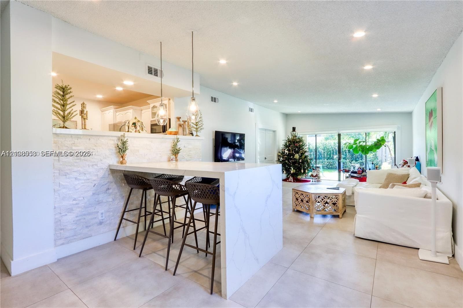 Kitchen island with a white stone-finish countertop, stacked stone facade, recessed lighting, and dual pendant light fixtures, finished with large-format tile flooring