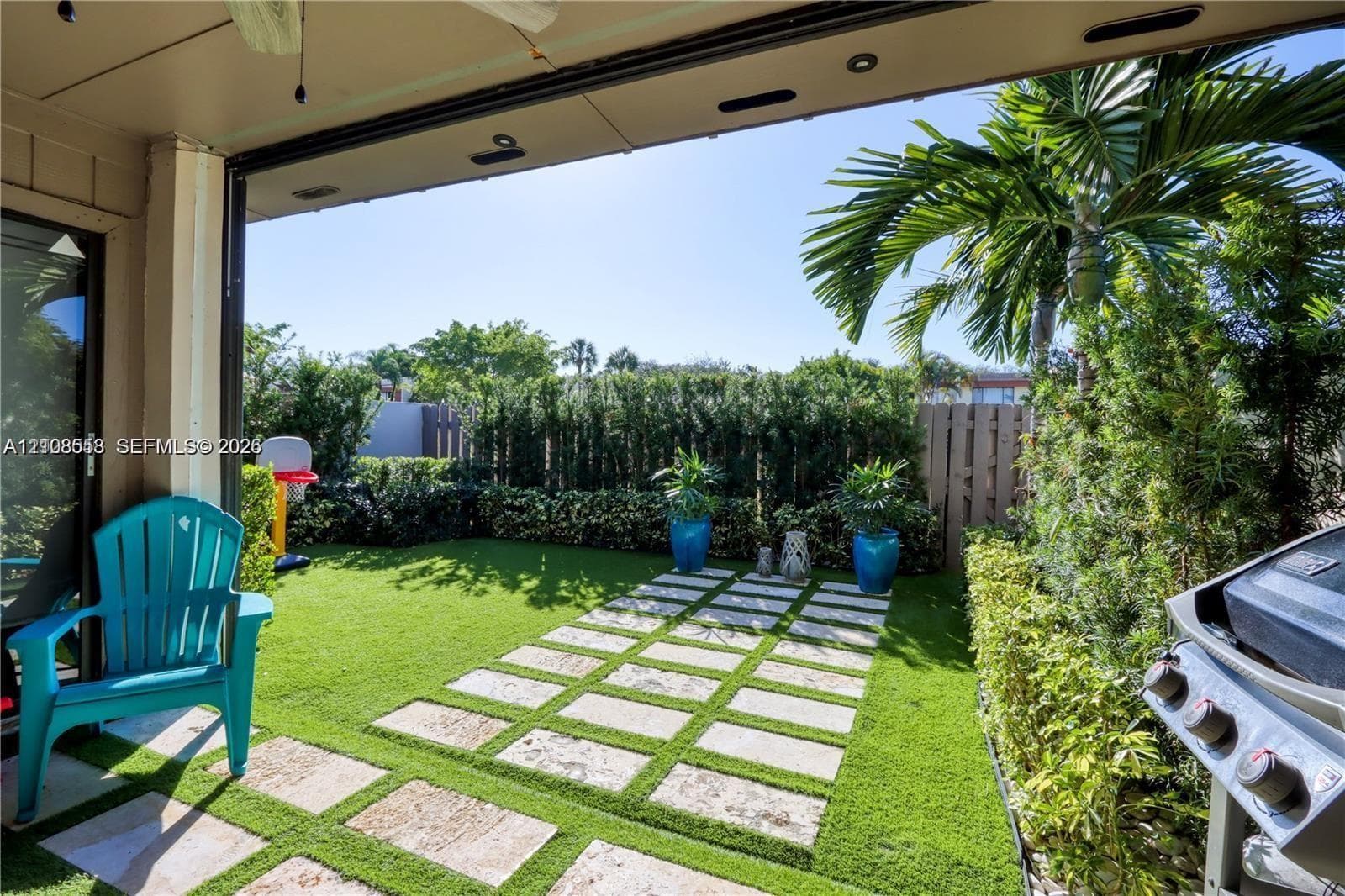 Covered patio featuring a paved walkway, synthetic turf, and perimeter privacy hedges