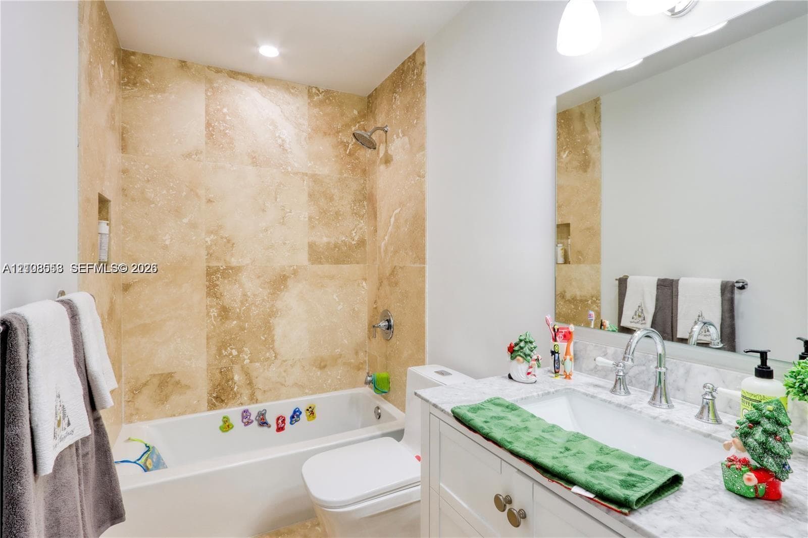 Bathroom featuring large-format natural stone wall tile, an undermount rectangular sink, a light-toned stone vanity countertop, white cabinetry with metallic hardware, and a large wall-mounted mirror