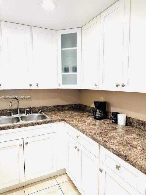 Kitchen featuring white shaker-style cabinetry, a glass-panel display cabinet, laminate countertops, a stainless steel double-basin sink, and tile flooring