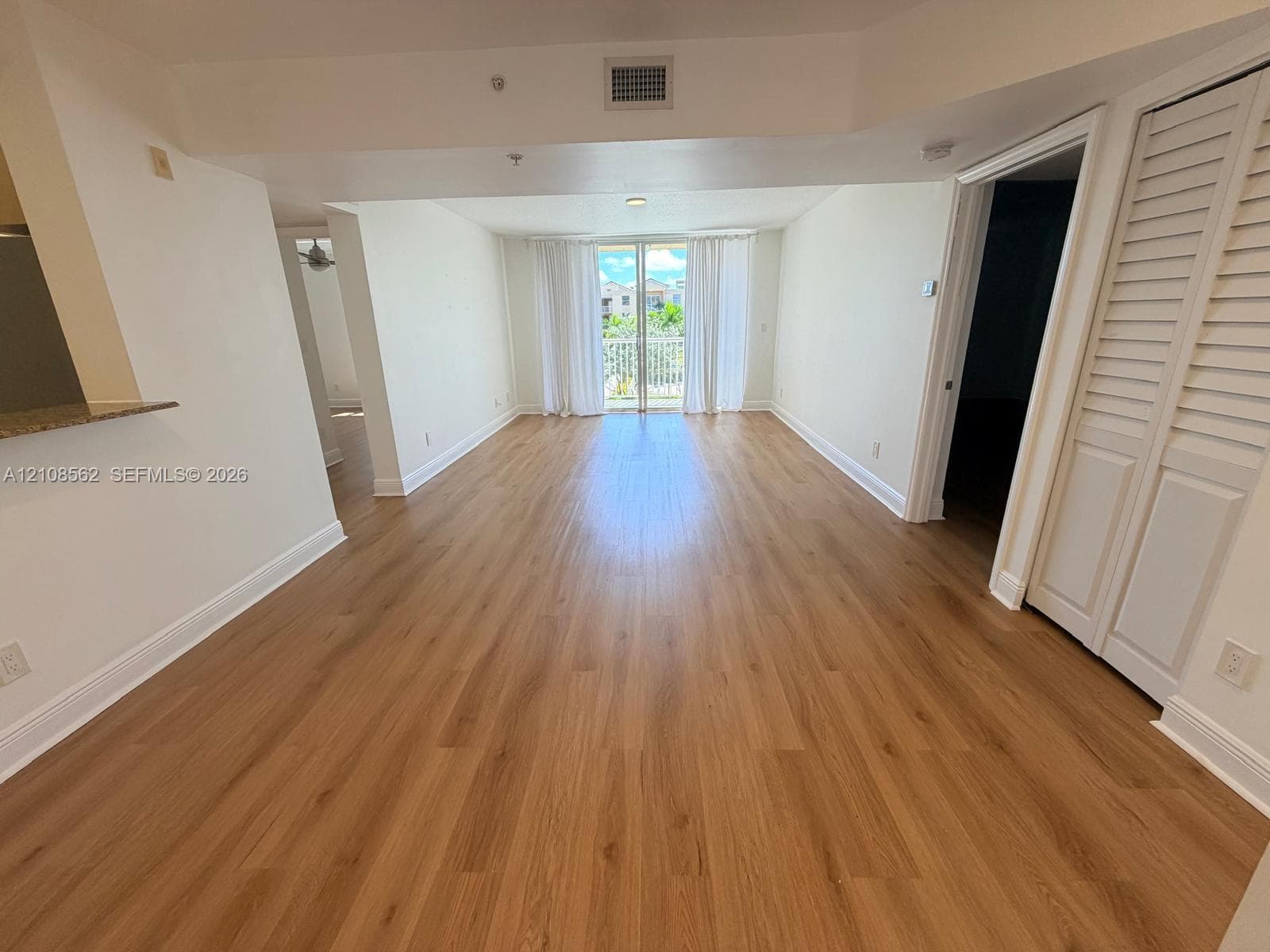 Open-concept interior featuring wood-finish flooring, louvered closet doors, and a glass-paneled sliding door opening to a balcony