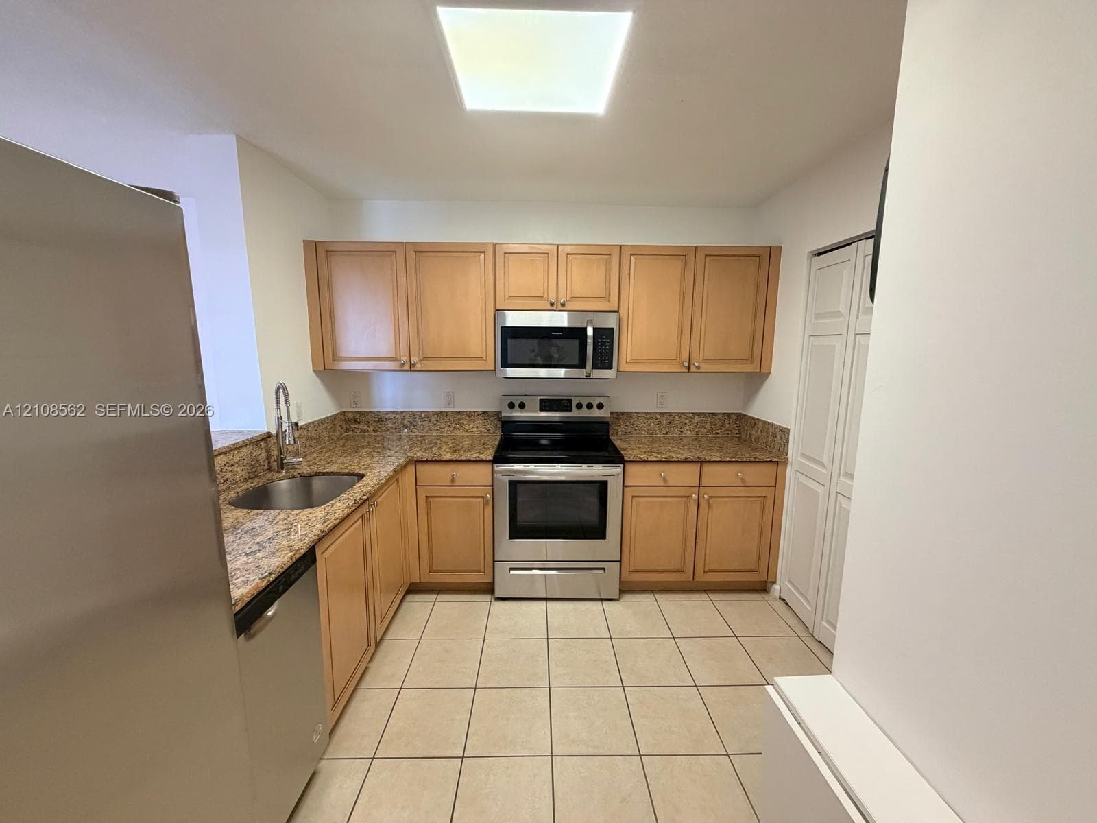 Kitchen featuring light wood cabinetry, stone-surface countertops, tile flooring, stainless steel appliances, and a recessed ceiling light