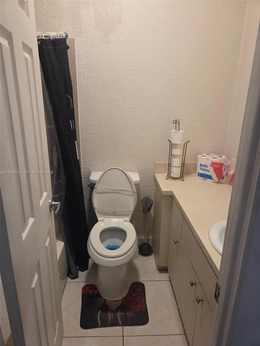 Bathroom featuring ceramic tile flooring, built-in cabinetry with a solid surface countertop, and a white porcelain sink and toilet