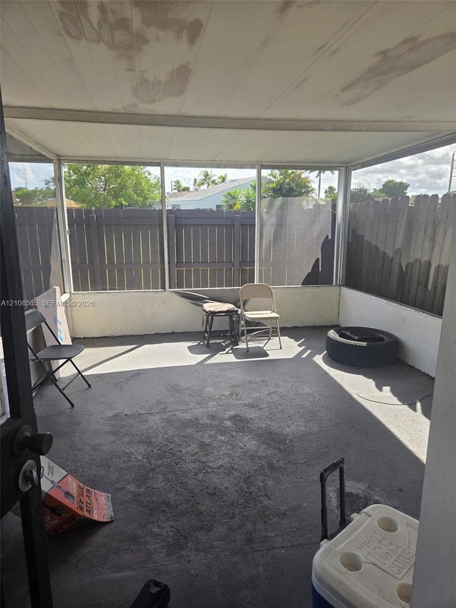 Enclosed porch featuring a concrete floor, screened-in walls, a solid roof, and a wooden privacy fence