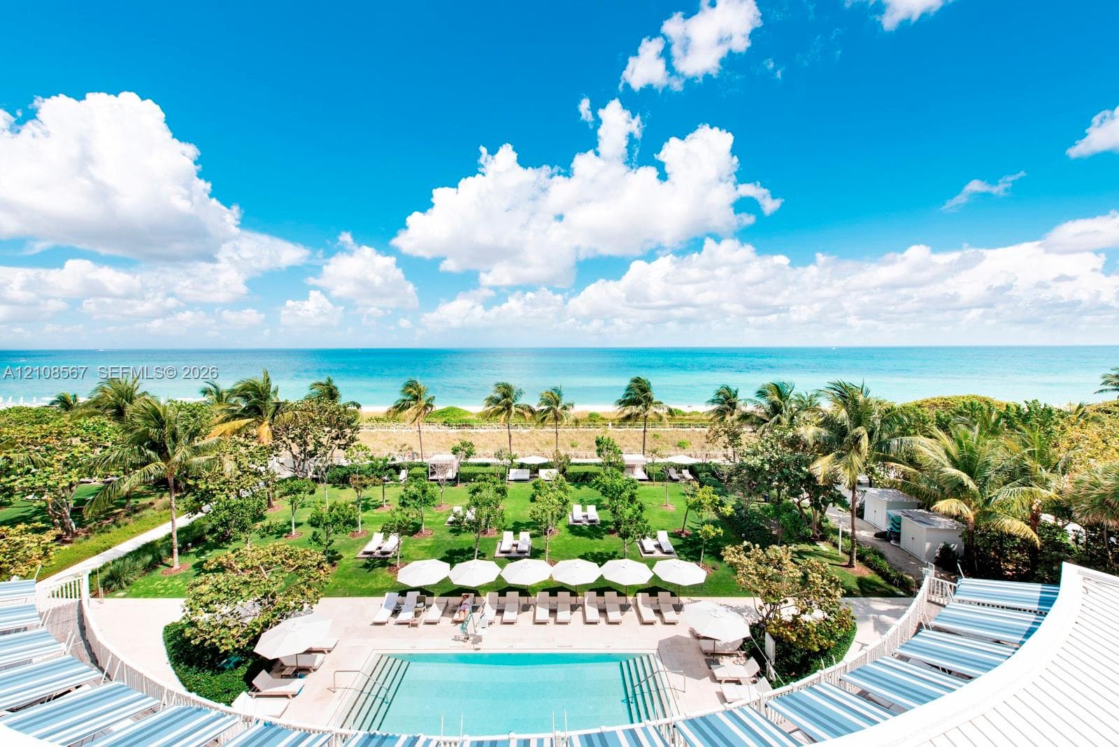 Outdoor swimming pool with integrated steps, paved pool deck, manicured green space with mature palm trees, and direct oceanfront positioning