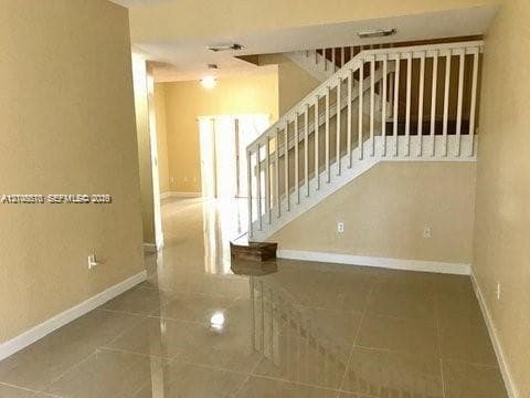 Large-format tile flooring, staircase featuring white wooden balusters and handrails, and recessed ceiling lighting