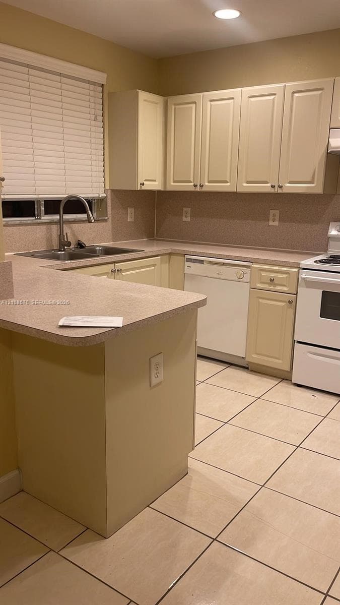 Kitchen featuring light-toned cabinetry, solid-surface countertops, tile flooring, a dual-basin stainless steel sink, and a built-in dishwasher