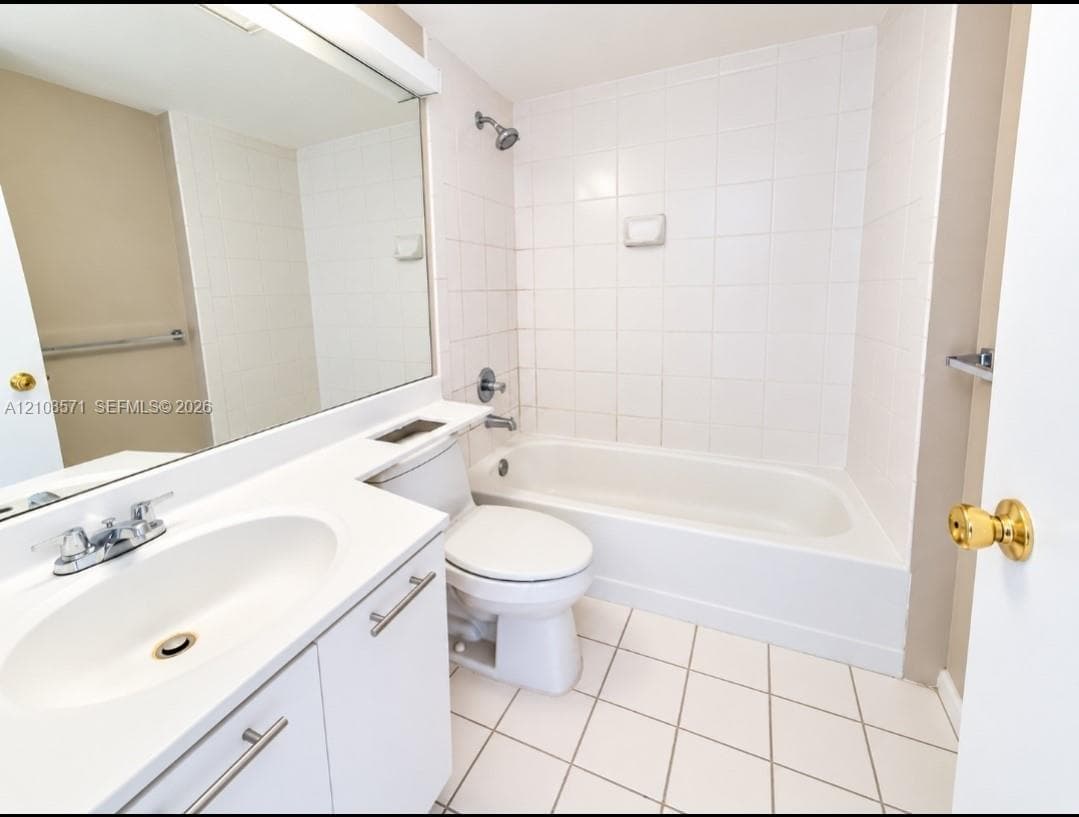 Bathroom featuring a white vanity with an integrated basin, wall-to-wall mirror, tiled shower and tub enclosure, and ceramic tile flooring