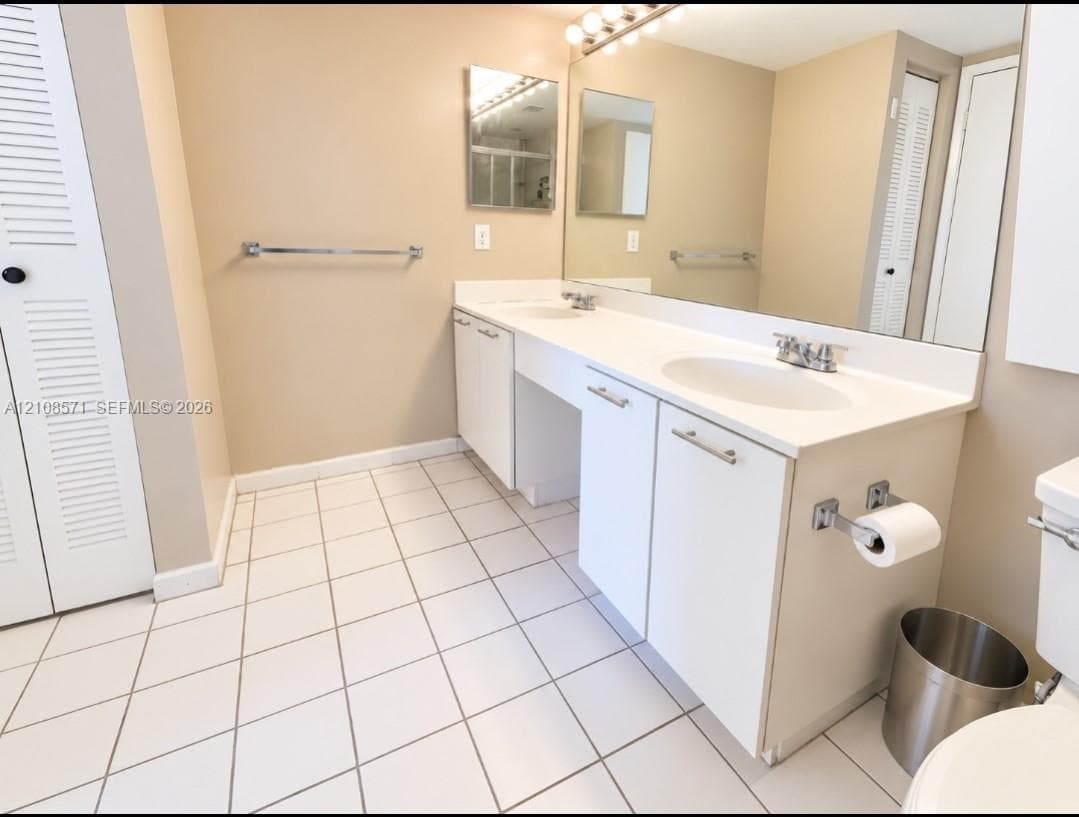 Double vanity featuring white cabinetry, integrated sinks, a full-width wall mirror, and white tile flooring