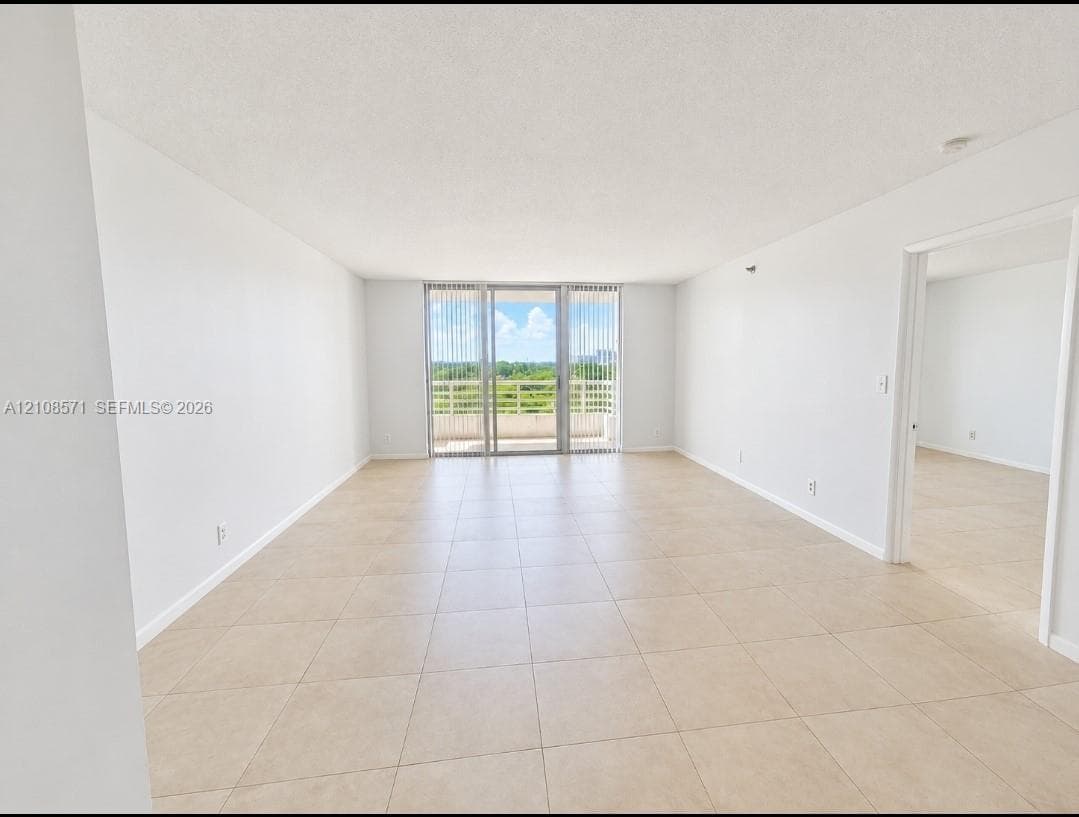 Neutral interior featuring light-toned tile flooring, floor-to-ceiling glass sliding doors, and a private balcony