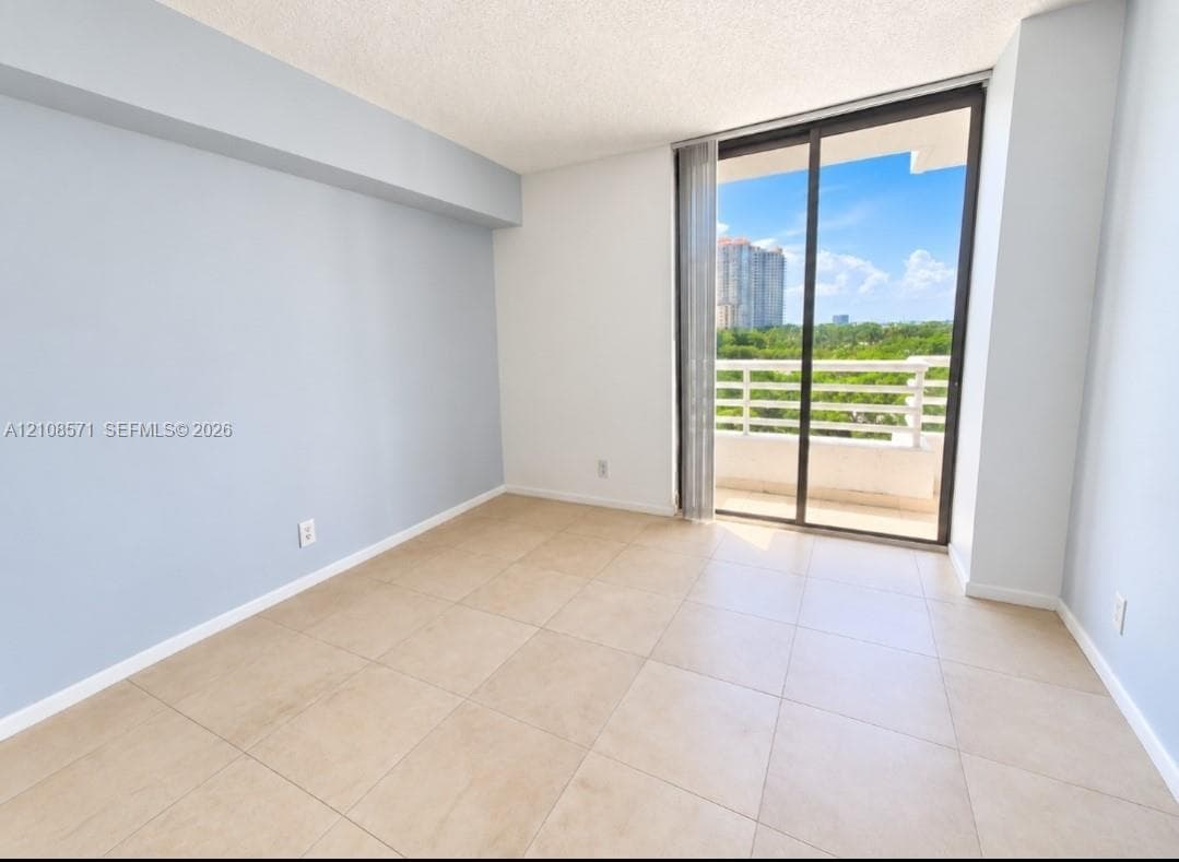 Large format neutral tile flooring, floor-to-ceiling glass sliding door, and private balcony with railing