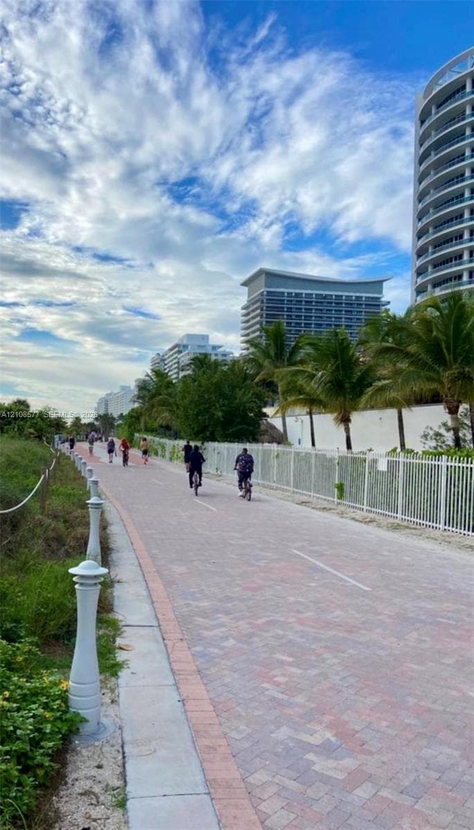 Paved multi-use trail featuring a brick-paver surface, decorative bollards, and perimeter fencing