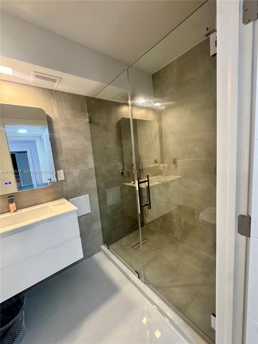 Bathroom featuring a wall-mounted floating vanity, rectangular integrated sink, glass-enclosed shower with large-format tile surround, and an illuminated medicine cabinet