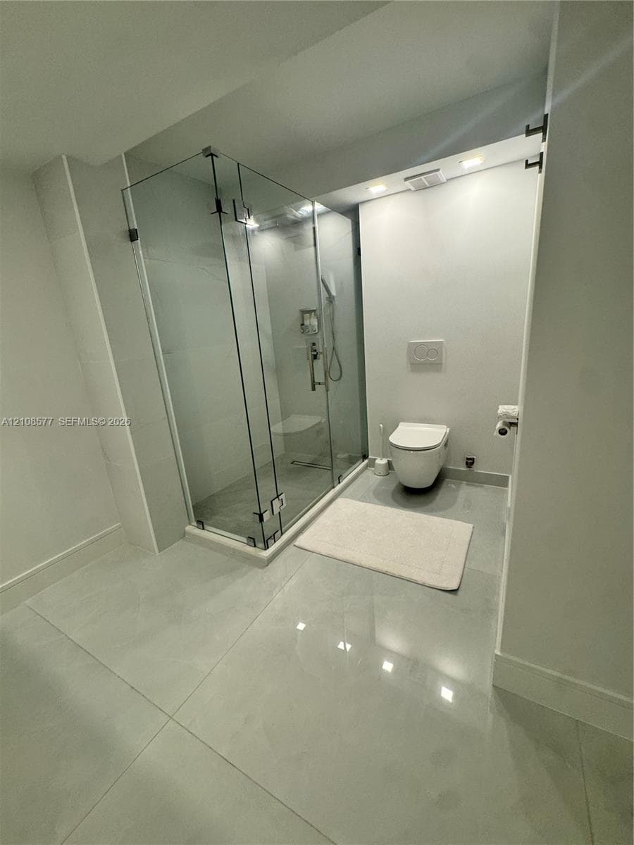Glass-enclosed shower with polished chrome fixtures, large-format tile flooring, and wall-mounted toilet