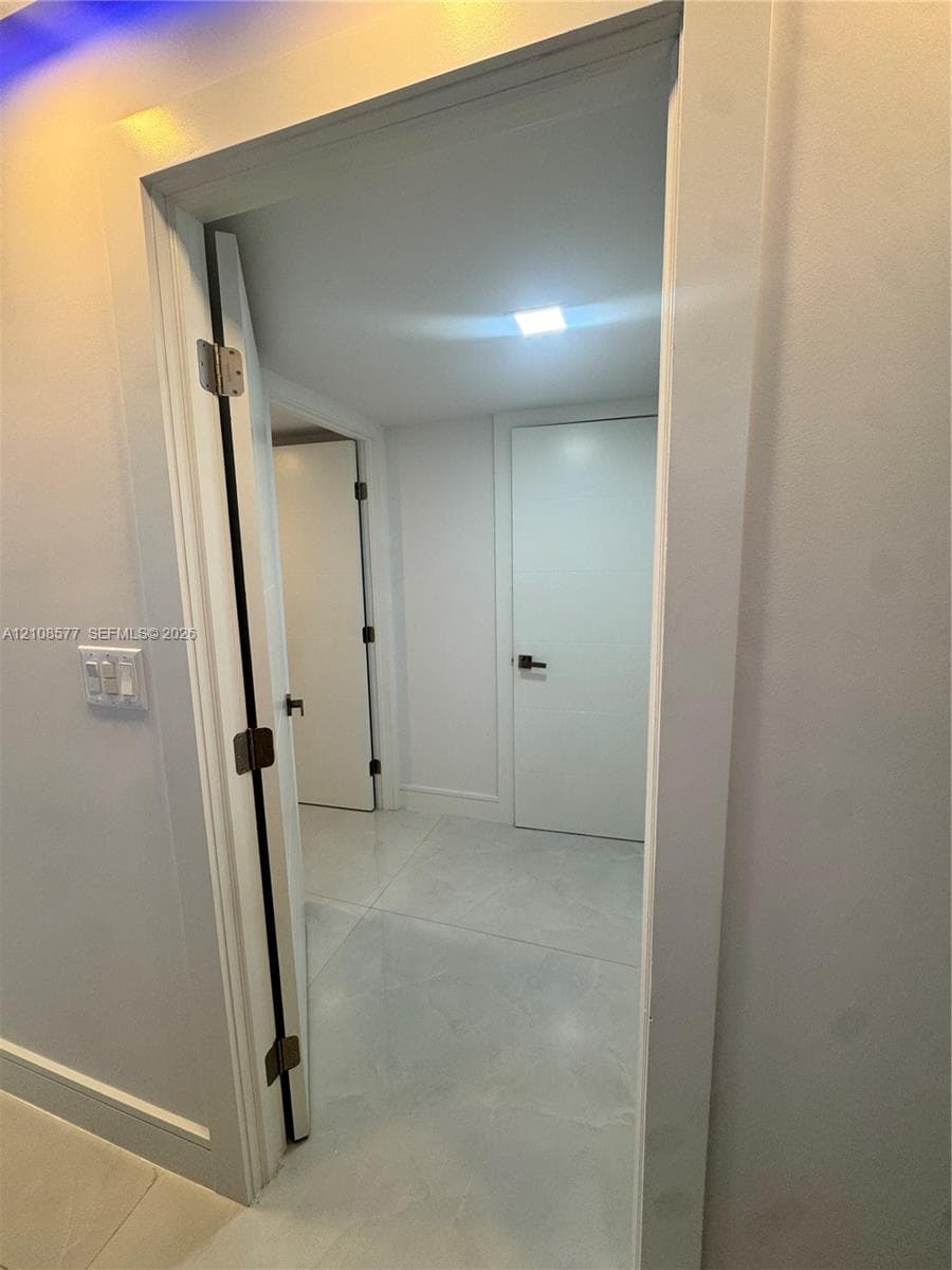 Interior hallway featuring large-format tile flooring, flat-panel doors, matte black hardware, and recessed LED ceiling lighting