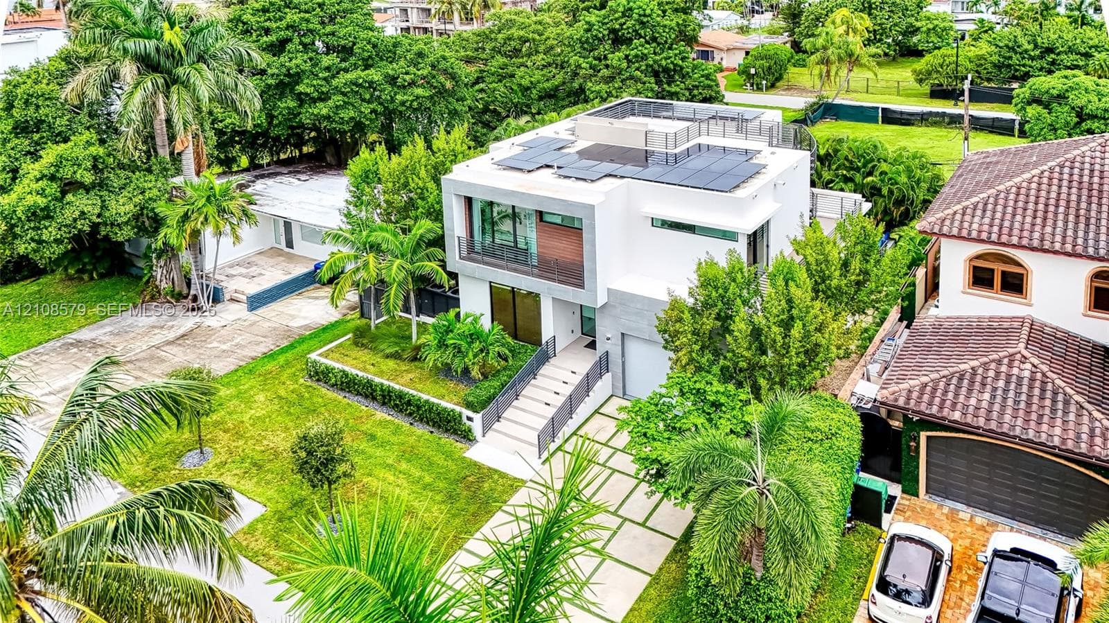 Modern two-story exterior featuring a white stucco facade, solar panel array, flat roof terrace, grid-pattern paver driveway, and metal railed balcony