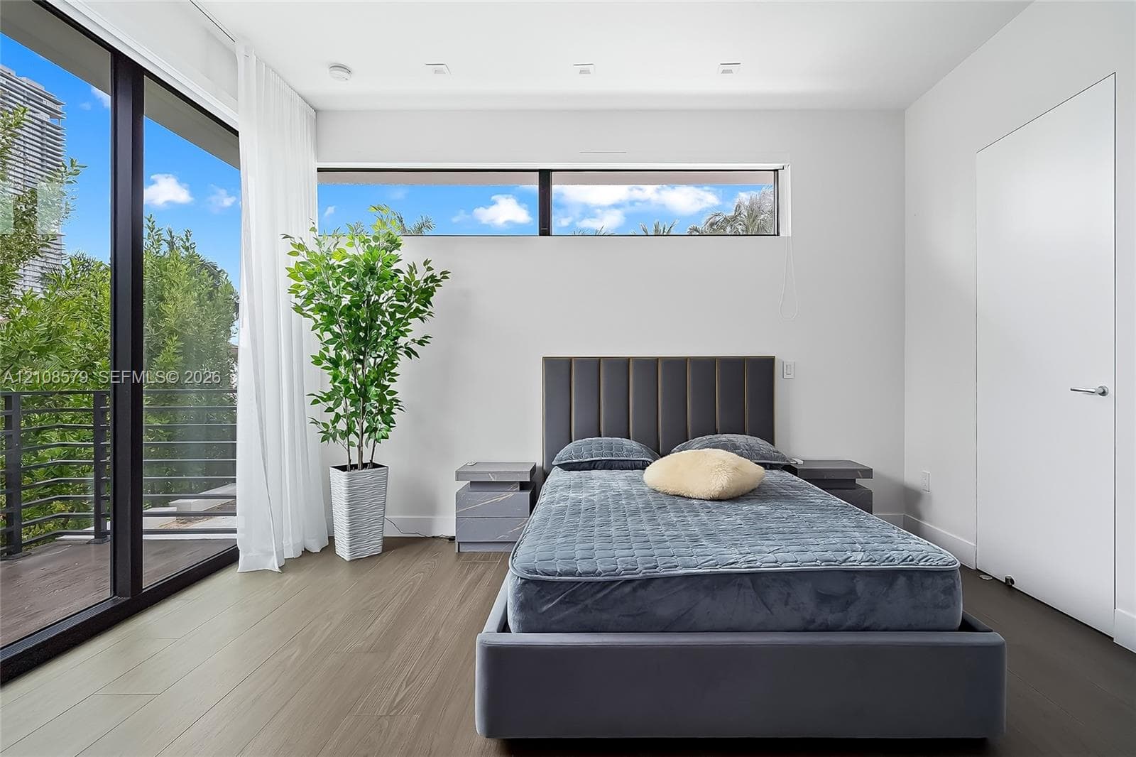 Floor-to-ceiling glass sliding doors, wood-finish flooring, recessed ceiling lighting, horizontal clerestory windows, and a private exterior balcony with metal railing