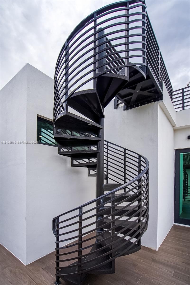 Spiral staircase featuring black metal construction with horizontal railing, smooth white stucco exterior walls, and wood-finish tile flooring
