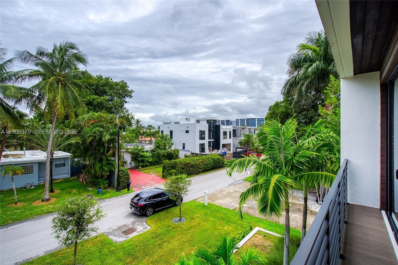 Covered balcony with composite decking and metal railings, overlooking a landscaped yard with mature palm trees
