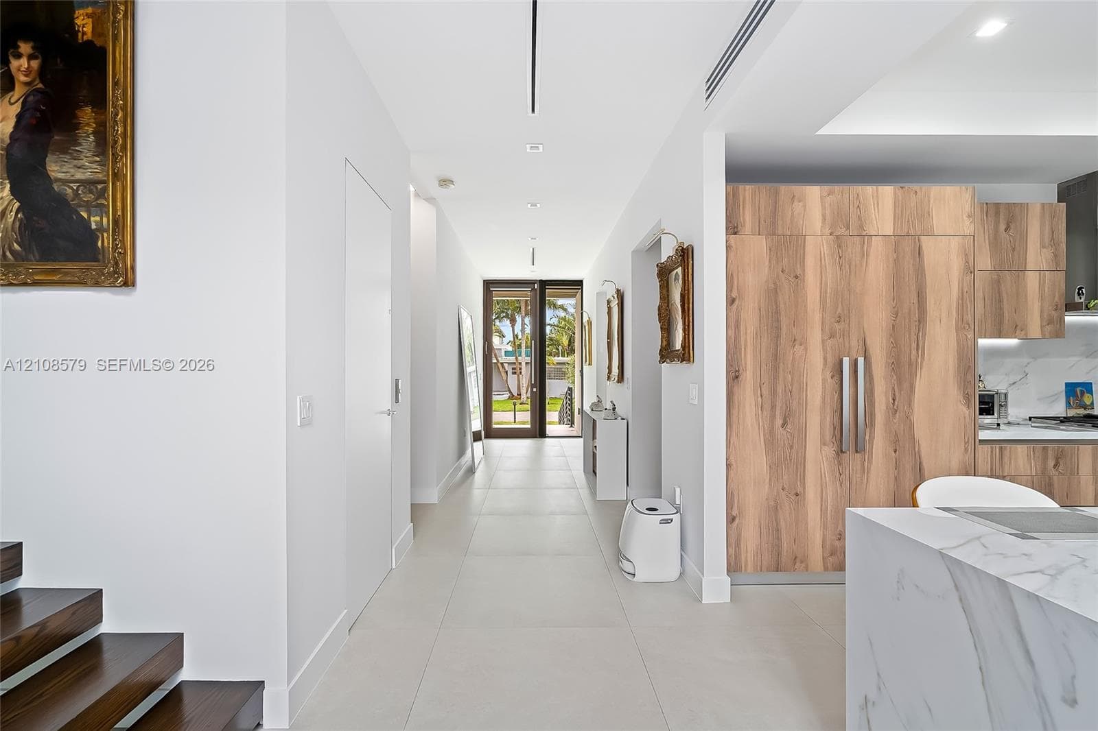 Large-format porcelain tile flooring, wood-finish cabinetry, stone-surface kitchen island with waterfall edge, and custom recessed linear lighting