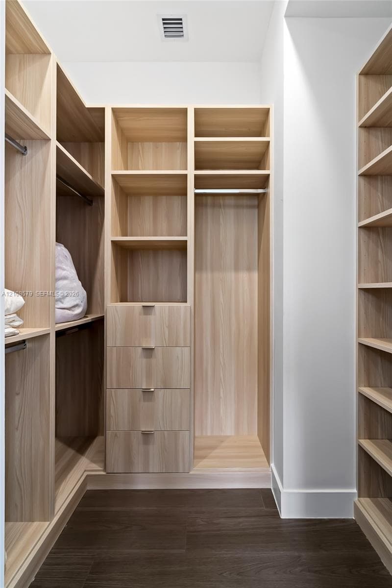 Custom wood-finish storage system featuring floor-to-ceiling shelving, integrated garment rods, four built-in drawers with metallic pulls, and dark wood-finish flooring
