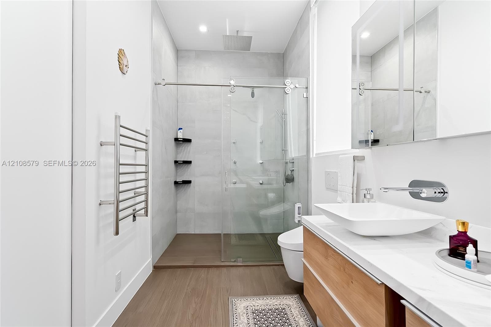 Modern bathroom featuring a wood-finish floating vanity with a rectangular vessel sink, wall-mounted chrome faucet, glass-enclosed walk-in shower with rainfall showerhead, and a wall-mounted heated towel rack