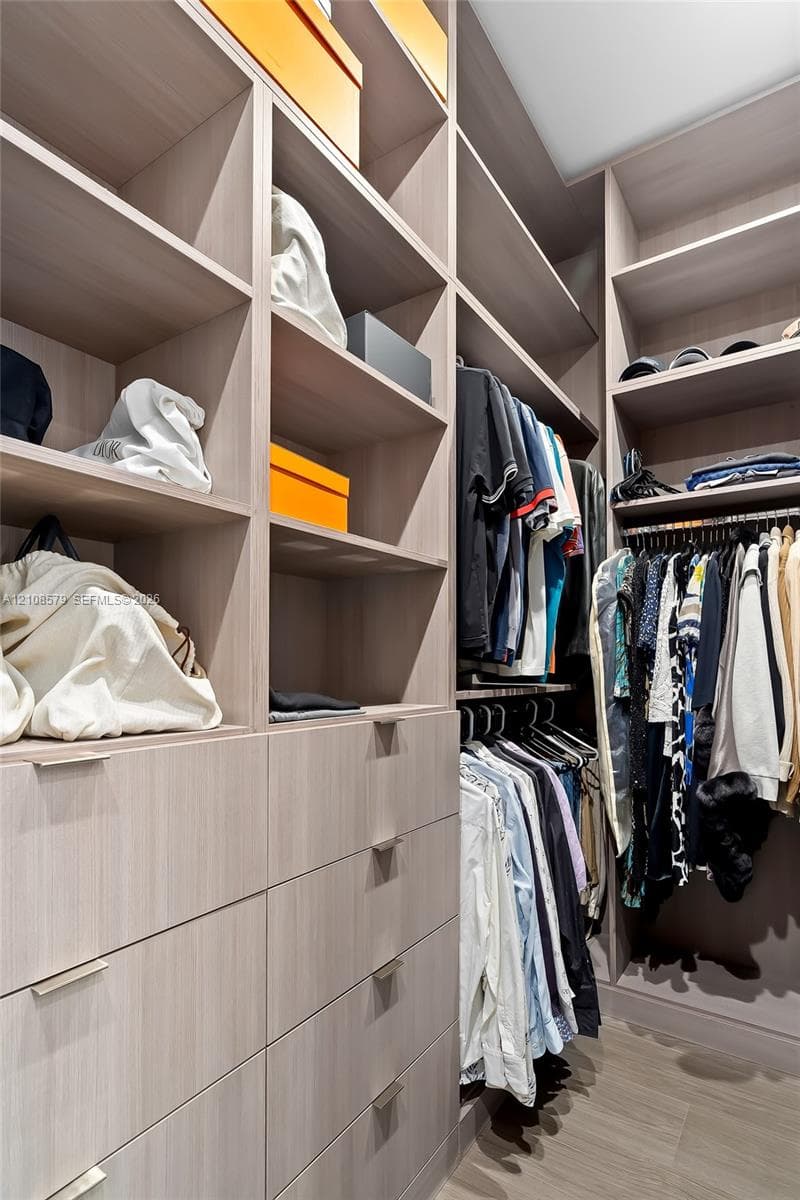 Custom wood-finish cabinetry featuring floor-to-ceiling shelving, multiple integrated storage drawers, horizontal metallic pulls, and built-in hanging rods
