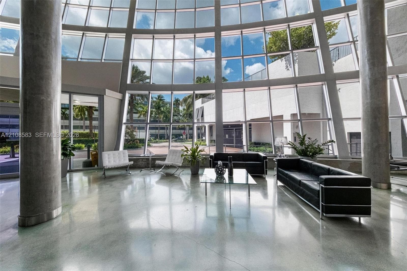 Grand two-story floor-to-ceiling glass wall, polished concrete flooring, and cylindrical structural columns