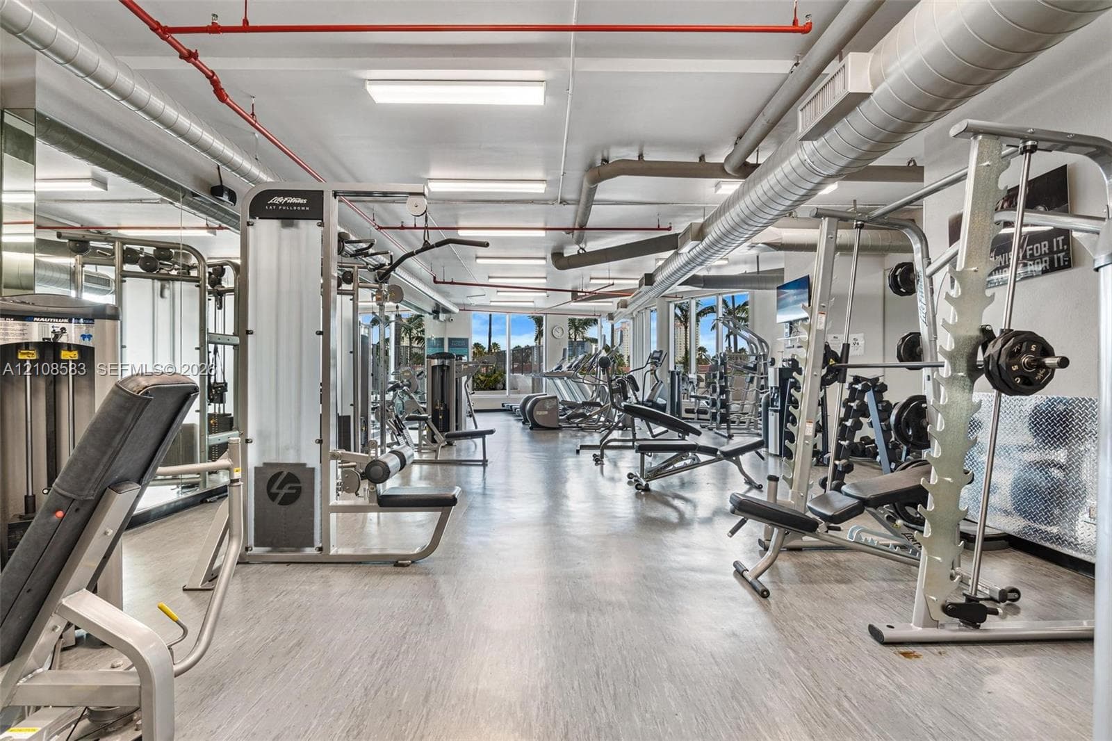 Fitness center featuring industrial-style exposed ductwork, large-format tile flooring, recessed overhead lighting, and floor-to-ceiling windows