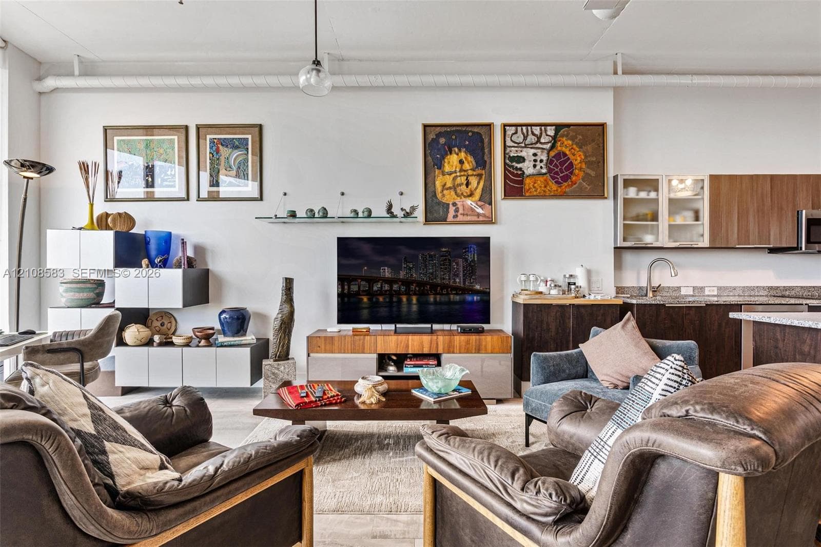 Open-concept interior featuring exposed industrial piping, flat-panel cabinetry with glass-front uppers, and solid-surface countertops