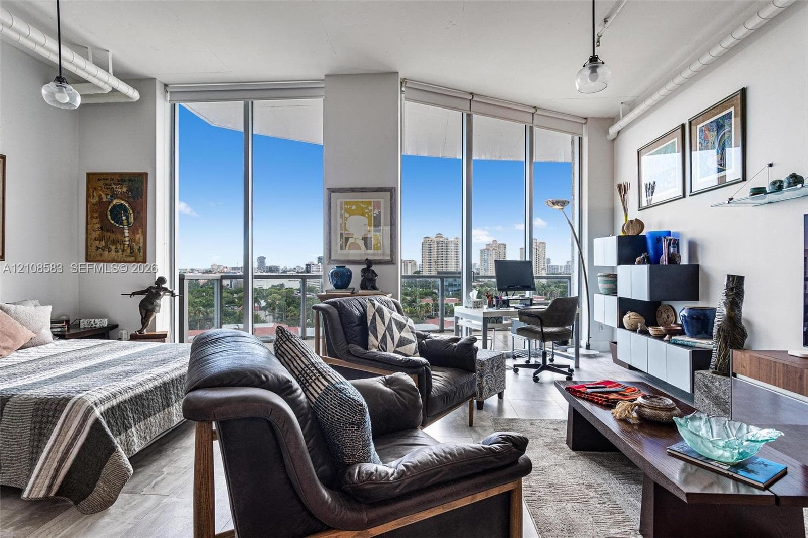 Floor-to-ceiling windows, wood-finish flooring, exposed white overhead piping, and modern pendant lighting