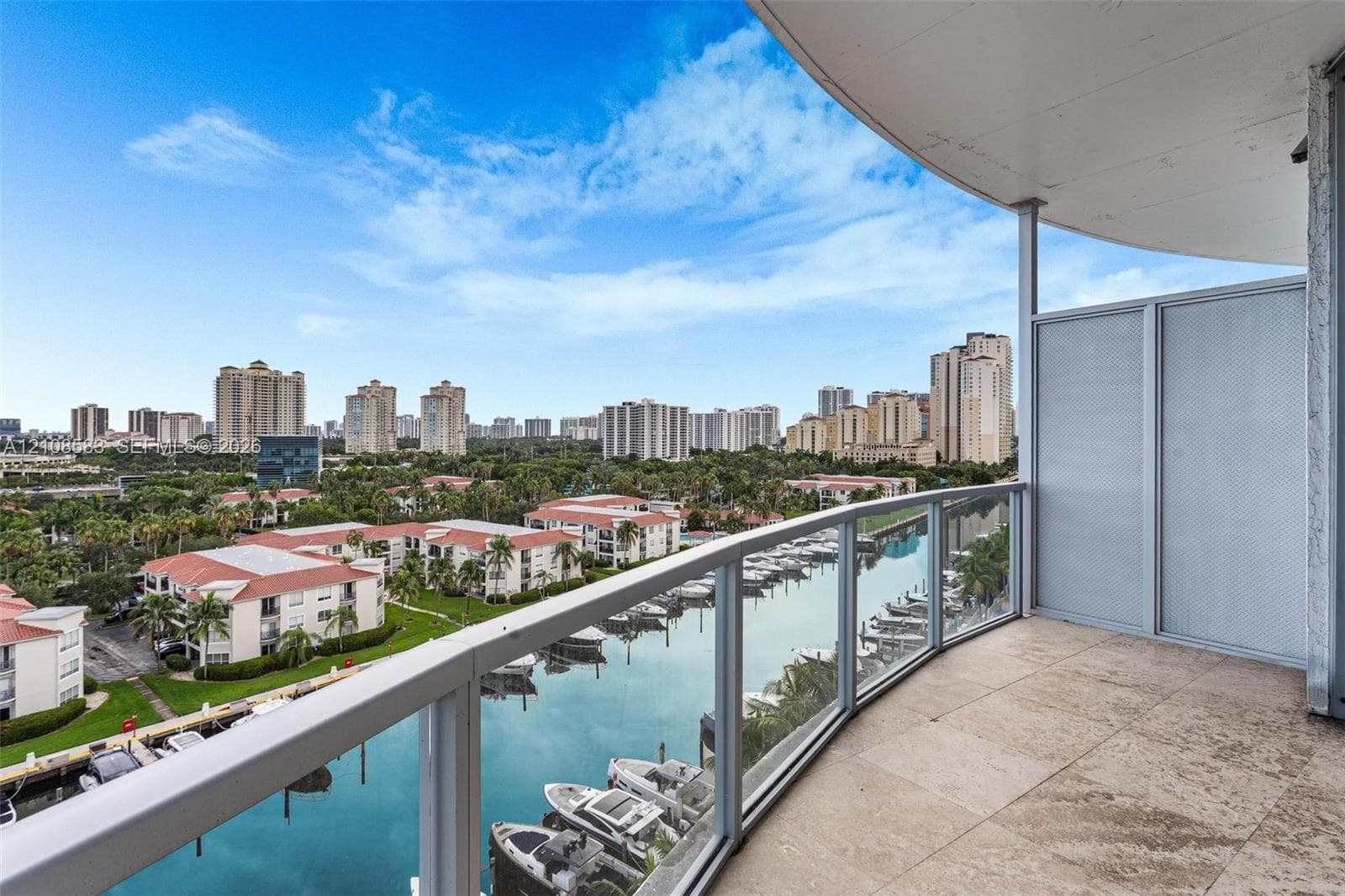 Covered balcony featuring stone flooring and a glass-paneled railing overlooking the waterway and marina
