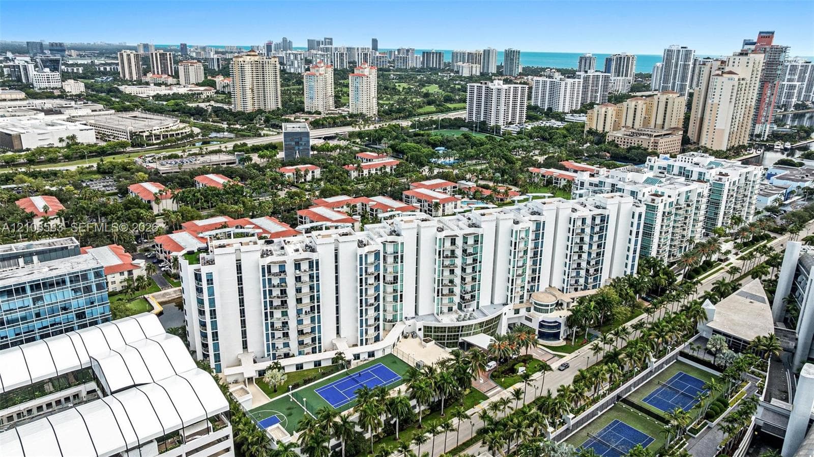 Aerial perspective of the high-rise residential complex featuring multiple hard-surface tennis courts, landscaped grounds, and a central entryway