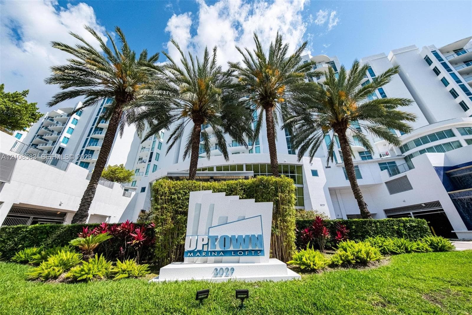 Multi-story residential building with white facade, private balconies, integrated landscaping, and palm trees
